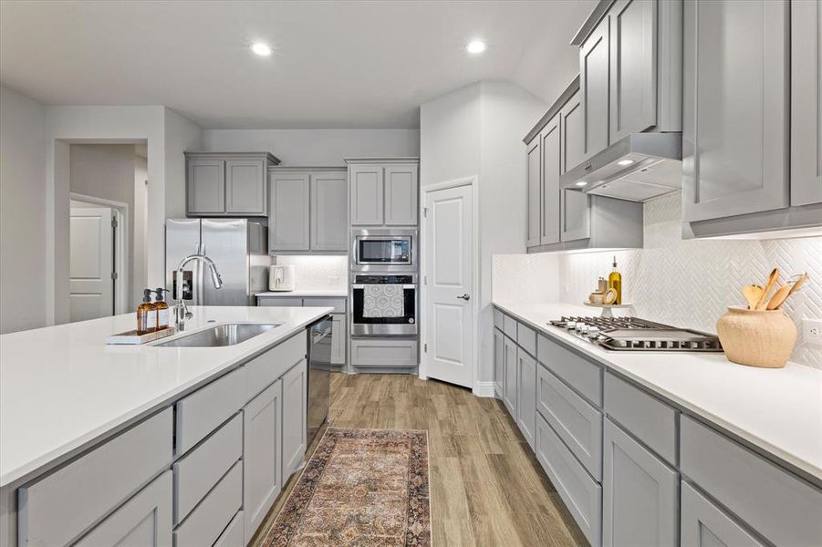 Kitchen with stainless steel appliances, wall chimney range hood, sink, gray cabinets, and light wood-type flooring