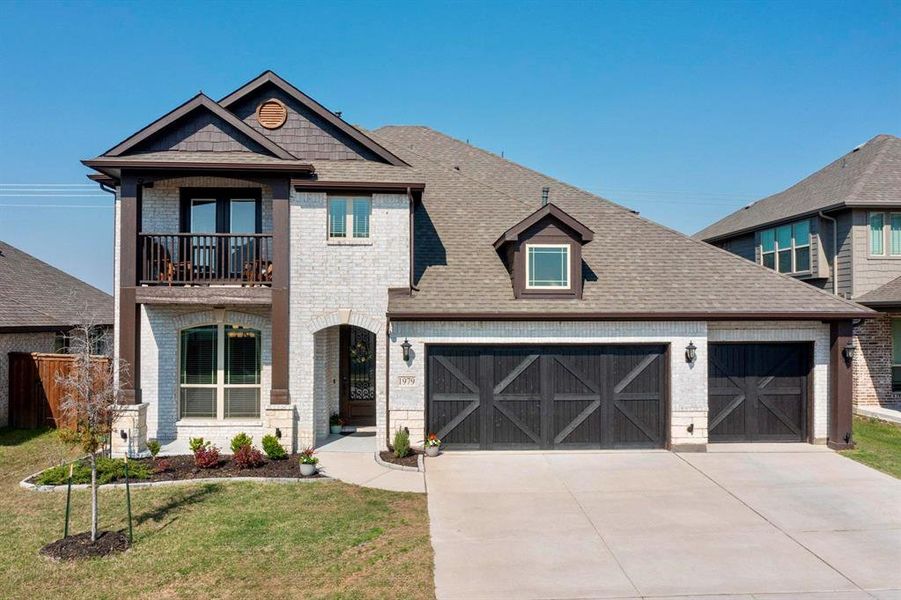 View of front facade featuring a shingled roof, a balcony, brick siding, concrete driveway, and an attached garage