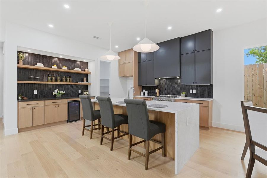 Modern kitchen featuring light wood-finish flooring, a white waterfall island, and dark-finish upper cabinetry Modern kitchen featuring light wood-finish flooring, a white waterfall island, and dark-finish upper cabinetry