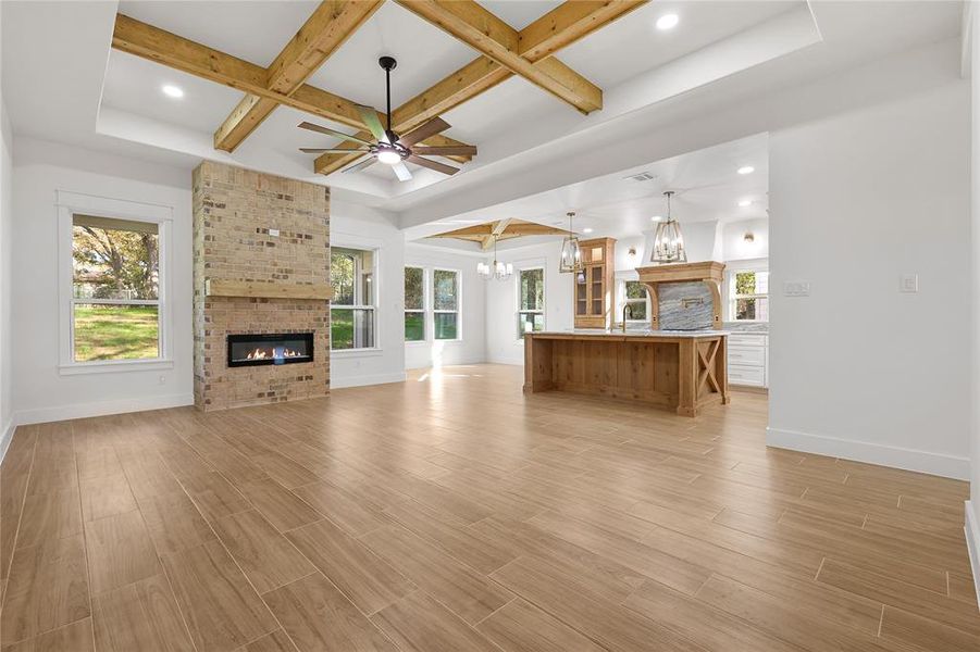 Unfurnished living room featuring a brick fireplace, ceiling fan, light wood-style floors, beam ceiling, and coffered ceiling