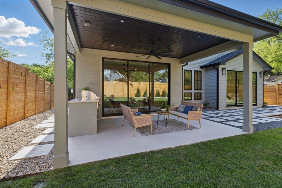 Fenced backyard with a ceiling fan, a patio, an outdoor hangout area, and exterior kitchen