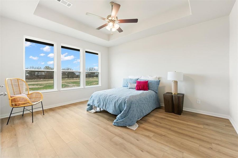 Bedroom with a tray ceiling, ceiling fan, and light wood-style floors