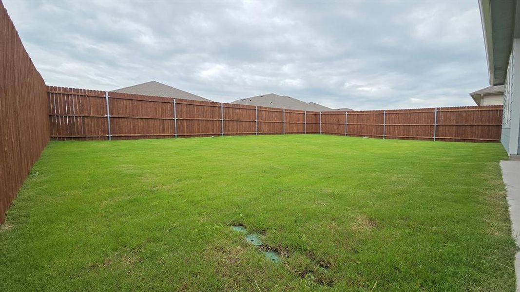 Expansive backyard featuring a lush green lawn, full wood privacy fencing, and a concrete patio area