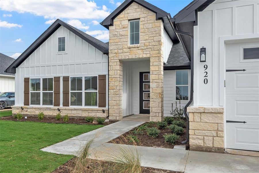View of front of property featuring stone siding, board and batten siding, roof with shingles, and a front yard View of front of property featuring stone siding, board and batten siding, roof with shingles, and a front yard