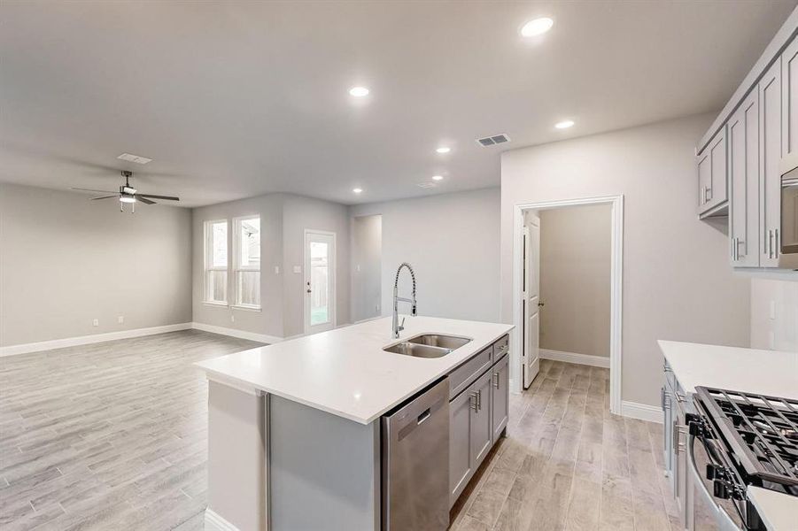 Kitchen with gray cabinetry, sink, stainless steel appliances, an island with sink, and light hardwood / wood-style floors