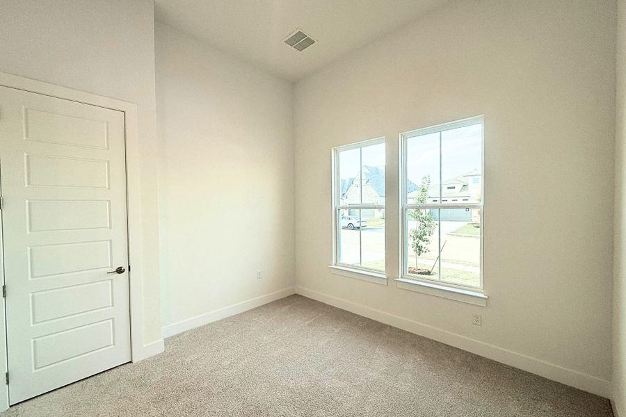 Bright interior room featuring two large windows, neutral-toned carpeting, white baseboards, and a five-panel interior door