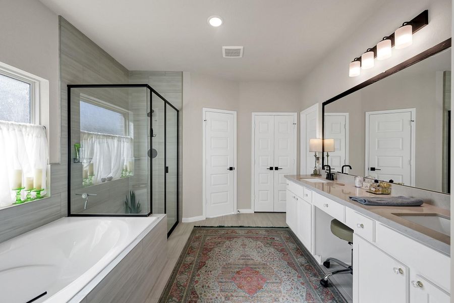 Primary bathroom featuring soaking tub, separate shower, two sinks, walk-in-closet and a closed off toilet room.