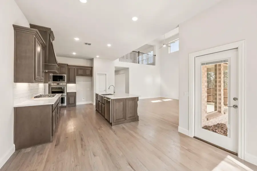 Open kitchen with dark brown cabinets, center island with sink, stainless appliances, and light hardwood floors