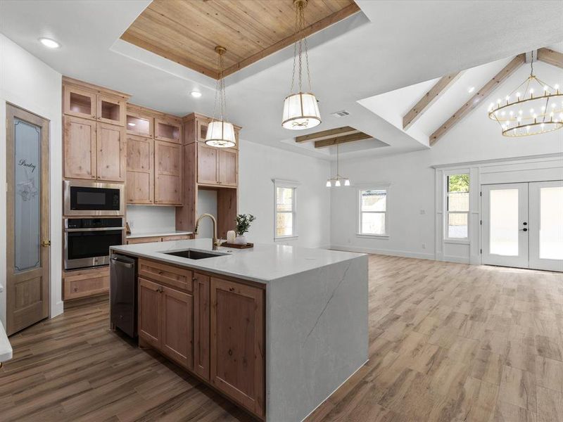 Kitchen with a chandelier, a tray ceiling, a kitchen island with sink, glass insert cabinets, and appliances with stainless steel finishes