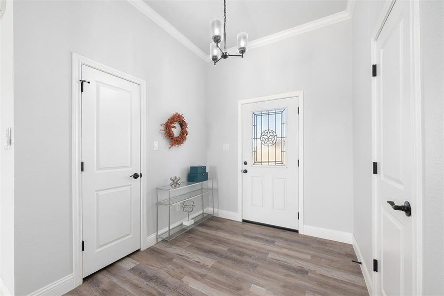 Entryway with an inviting chandelier, ornamental molding, and hardwood / wood-style floors