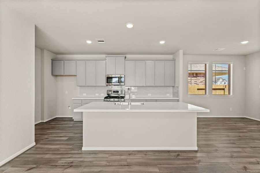 This light and bright kitchen features a large quartz island, white cabinets, a large sink overlooking your family room, recessed lighting, and beautiful backsplash.