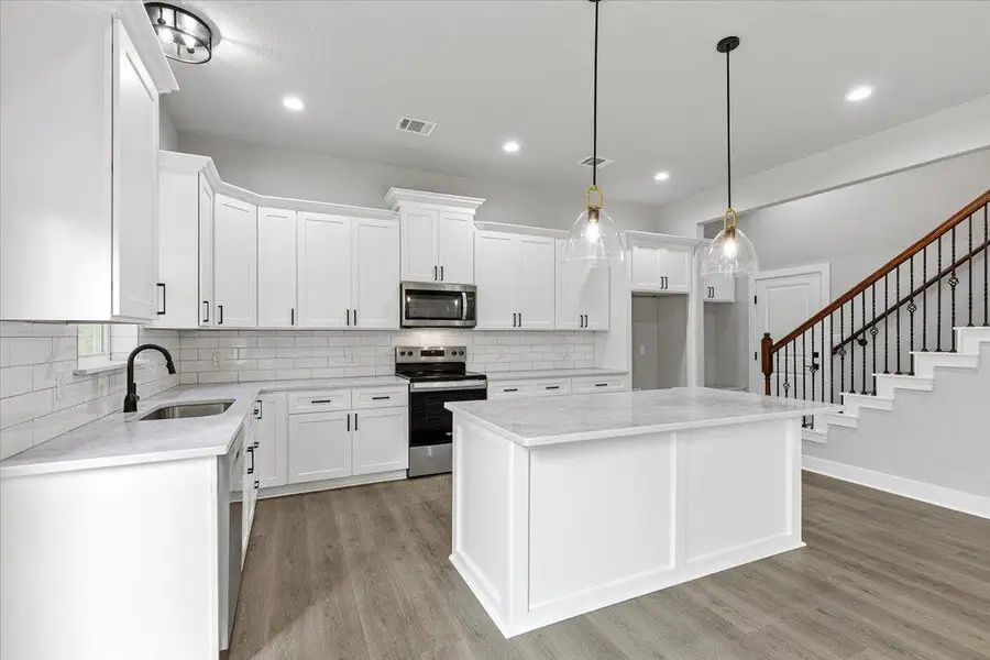 Modern kitchen with white cabinetry and a spacious island flows into a chic stairway. Modern kitchen with white cabinetry and a spacious island flows into a chic stairway.