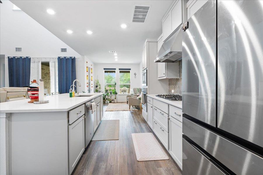 Kitchen featuring appliances with stainless steel finishes, open floor plan, white cabinetry, dark wood-style floors, and an island with sink