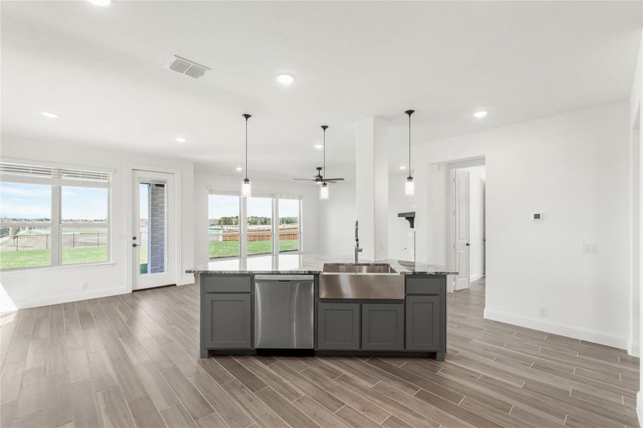 Kitchen island with gray cabinets, stainless steel farmhouse sink, and pendant lights over wood-look tile floors Kitchen island with gray cabinets, stainless steel farmhouse sink, and pendant lights over wood-look tile floors