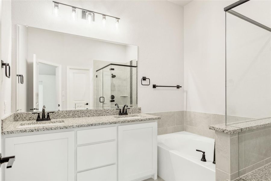 Bathroom with double vanity, granite countertops, soaking tub, and glass shower enclosure