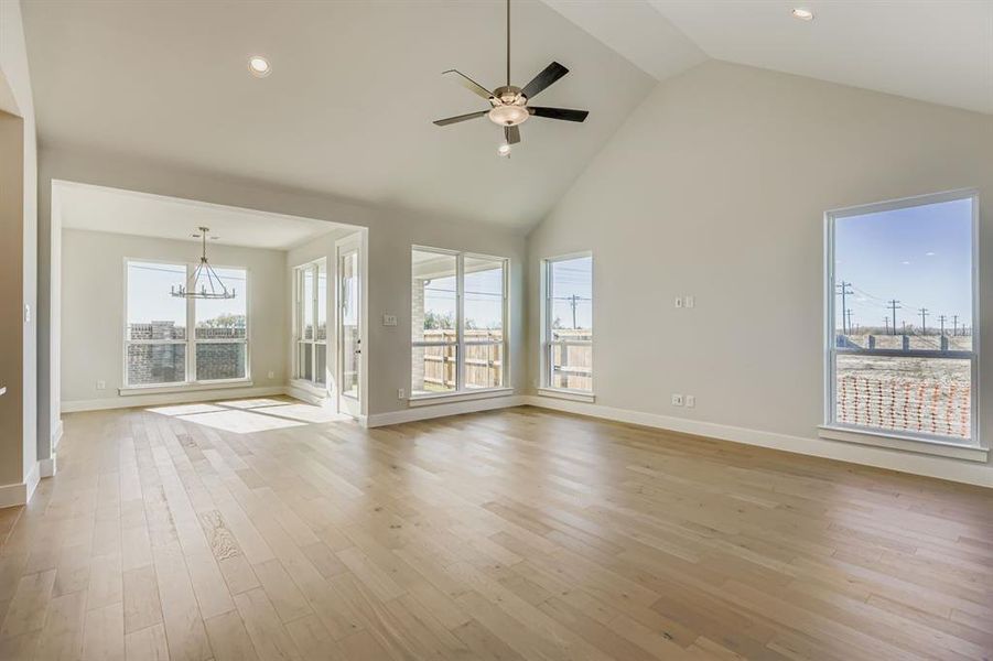Unfurnished living room with a chandelier, high vaulted ceiling, light wood-type flooring, recessed lighting, and ceiling fan