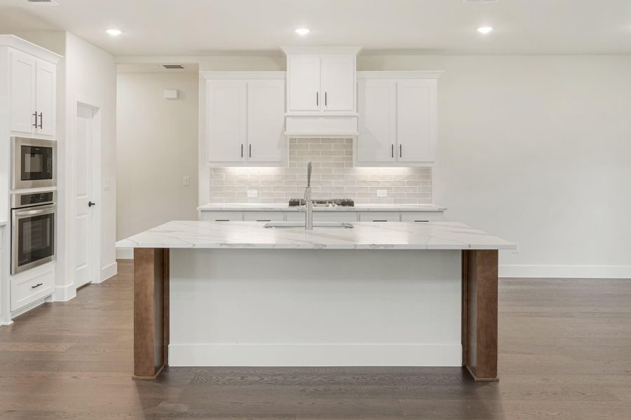 Kitchen with white cabinets, marble island, tile backsplash, and stainless steel double wall ovens on hardwood floors
