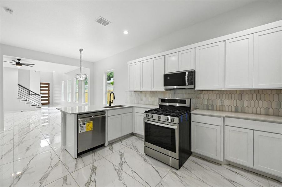 Kitchen with appliances with stainless steel finishes, a peninsula, decorative backsplash, white cabinets, and light marble finish floors