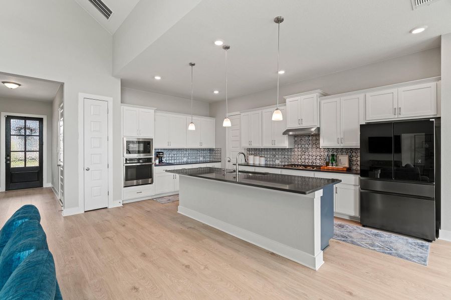 Kitchen with stainless steel appliances, a kitchen island with sink, white cabinetry, pendant lighting, and light wood-style floors Kitchen with stainless steel appliances, a kitchen island with sink, white cabinetry, pendant lighting, and light wood-style floors