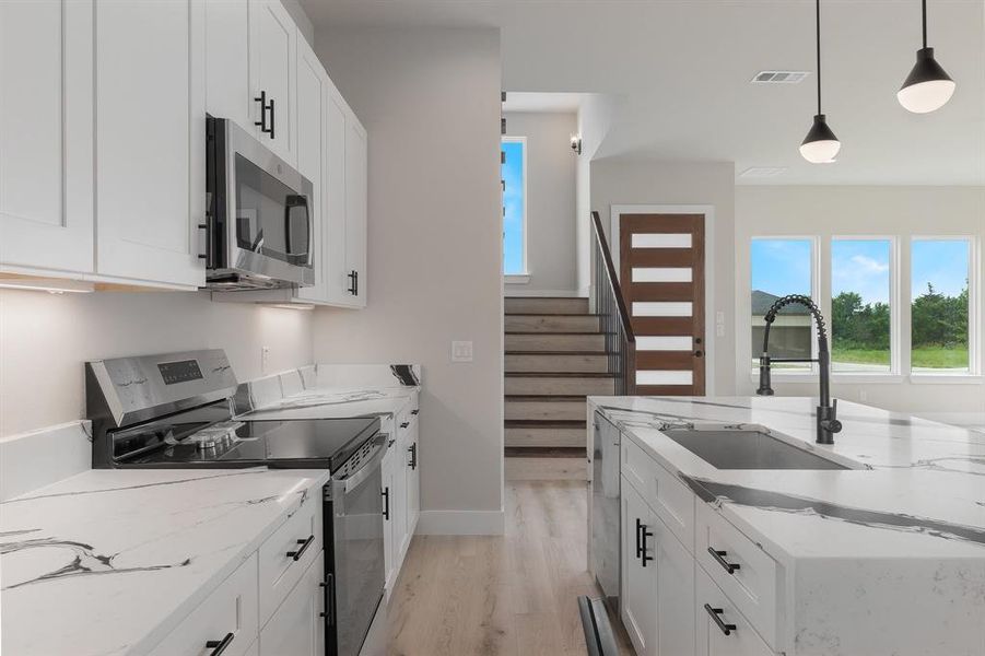 Kitchen with stainless steel appliances, a sink, light wood finished floors, white cabinetry, and light stone counters