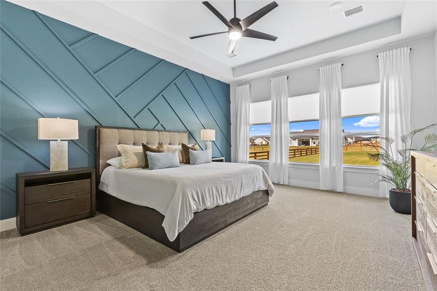 Bedroom with light colored carpet, a tray ceiling, a ceiling fan, and a decorative wall