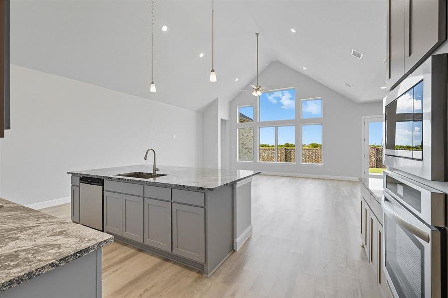 Kitchen with gray cabinets, high vaulted ceiling, dark stone countertops, stainless steel appliances, and a center island with sink Kitchen with gray cabinets, high vaulted ceiling, dark stone countertops, stainless steel appliances, and a center island with sink