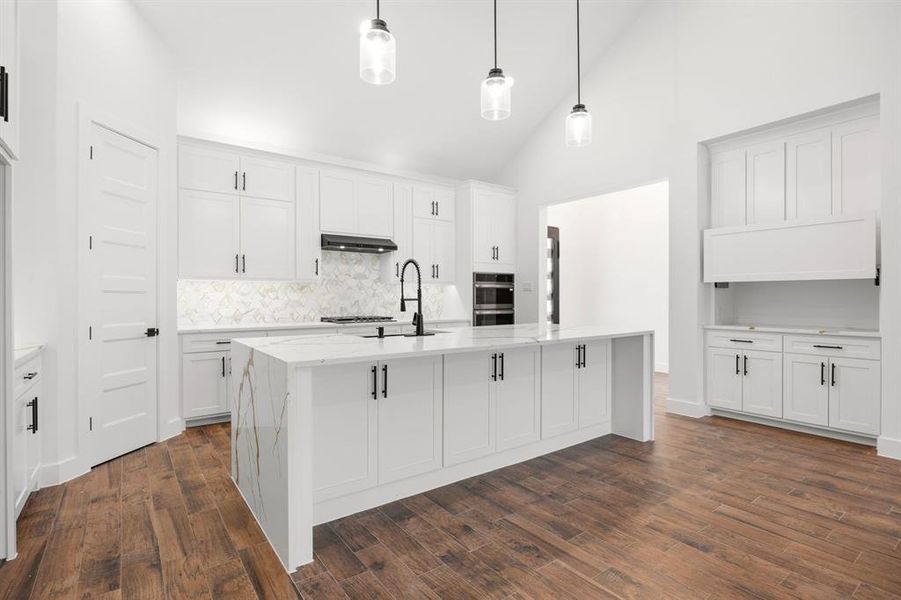 Modern kitchen featuring a waterfall island with a stone countertop, white shaker cabinetry, recessed lighting, and wood-finish flooring Modern kitchen featuring a waterfall island with a stone countertop, white shaker cabinetry, recessed lighting, and wood-finish flooring