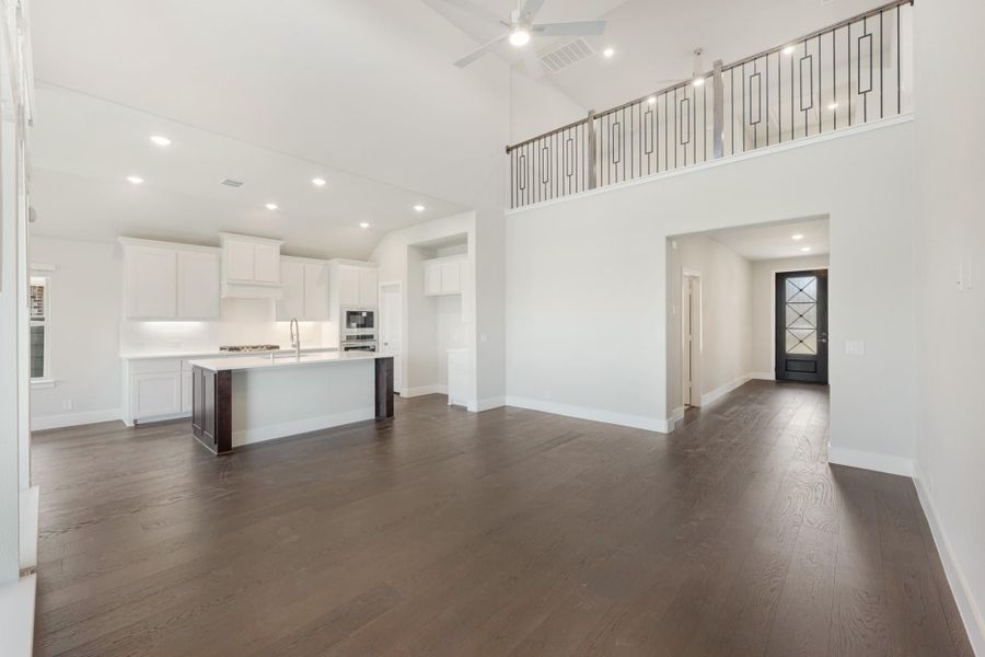 Open-concept living area with dark hardwood floors, high ceilings, and white kitchen with island visible in background Open-concept living area with dark hardwood floors, high ceilings, and white kitchen with island visible in background