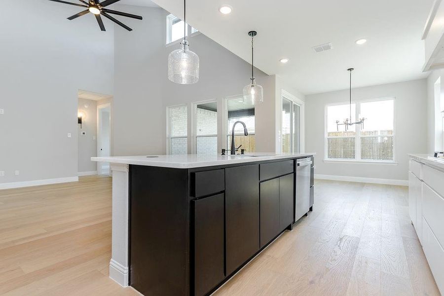 Kitchen with high vaulted ceiling, ceiling fan with notable chandelier, light hardwood / wood-style flooring, and a center island with sink