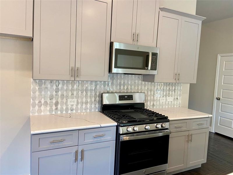 Kitchen featuring Monet Quartz countertops, decorative mosaic tile backsplash, and grey Shaker cabinets