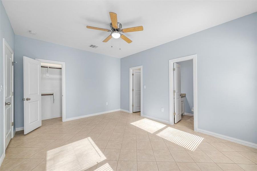 Unfurnished bedroom with ensuite bathroom, ceiling fan, a spacious closet, light tile patterned floors, and a closet