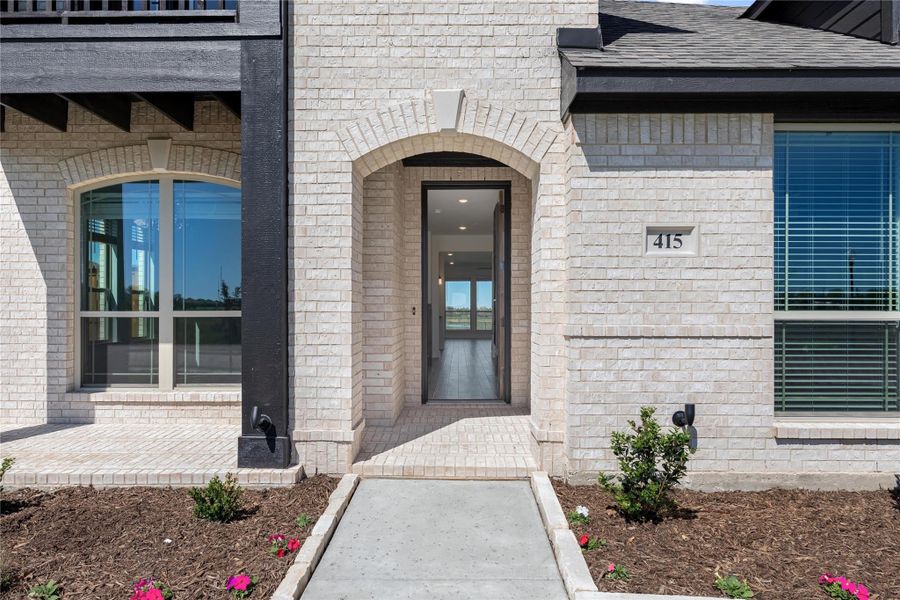 Home entrance with arched brick surround, open front door, and concrete walkway leading to entry Home entrance with arched brick surround, open front door, and concrete walkway leading to entry