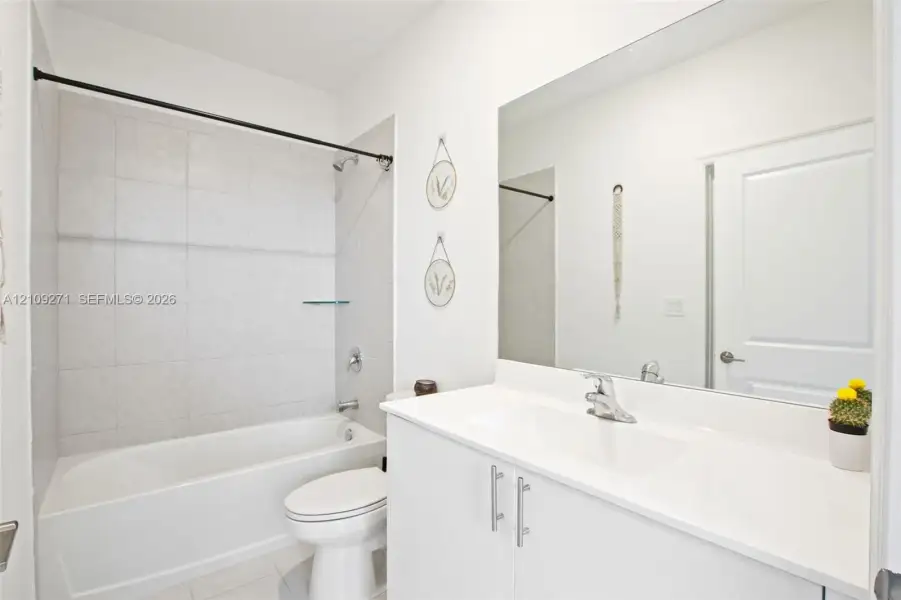 Bathroom featuring a vanity with a white countertop and integrated sink, full-width wall mirror, and a tub-shower combination with light-toned wall tile