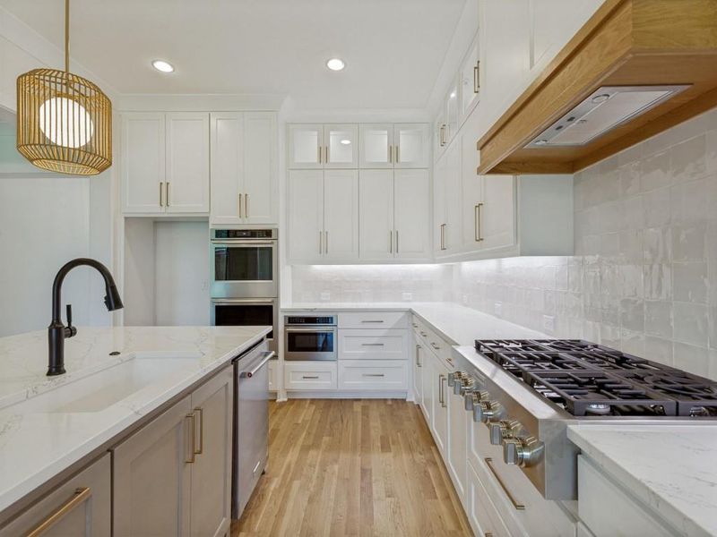 Modern kitchen featuring an integrated gas range, stainless steel appliances, and wood-finish flooring Modern kitchen featuring an integrated gas range, stainless steel appliances, and wood-finish flooring