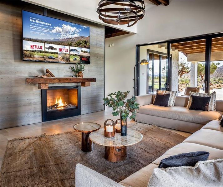 Living area with beam ceiling, a warm lit fireplace, and an inviting chandelier