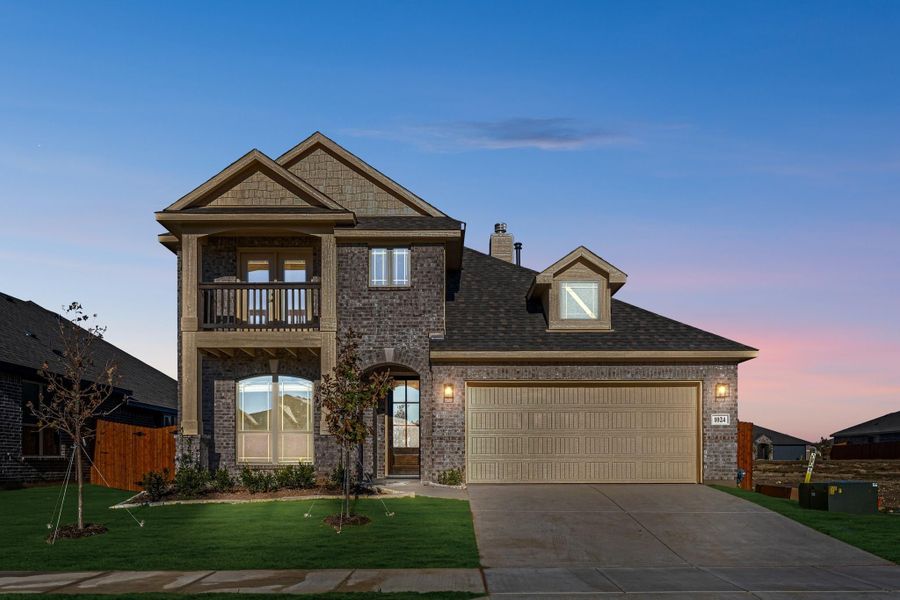 Two-story brick home with second-floor balcony, arched entry, and two-car garage at dusk Two-story brick home with second-floor balcony, arched entry, and two-car garage at dusk