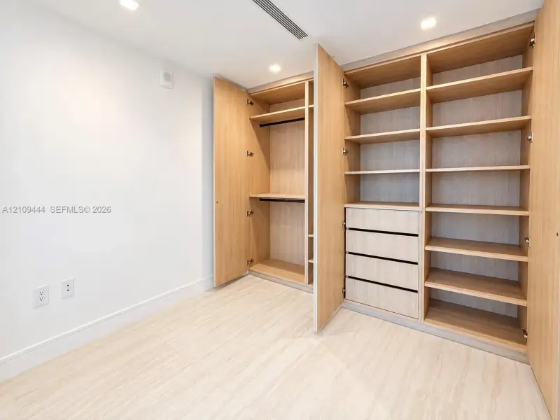 Custom built-in closet featuring light wood-finish shelving, hanging rods, and integrated drawers with recessed lighting and light wood-finish flooring