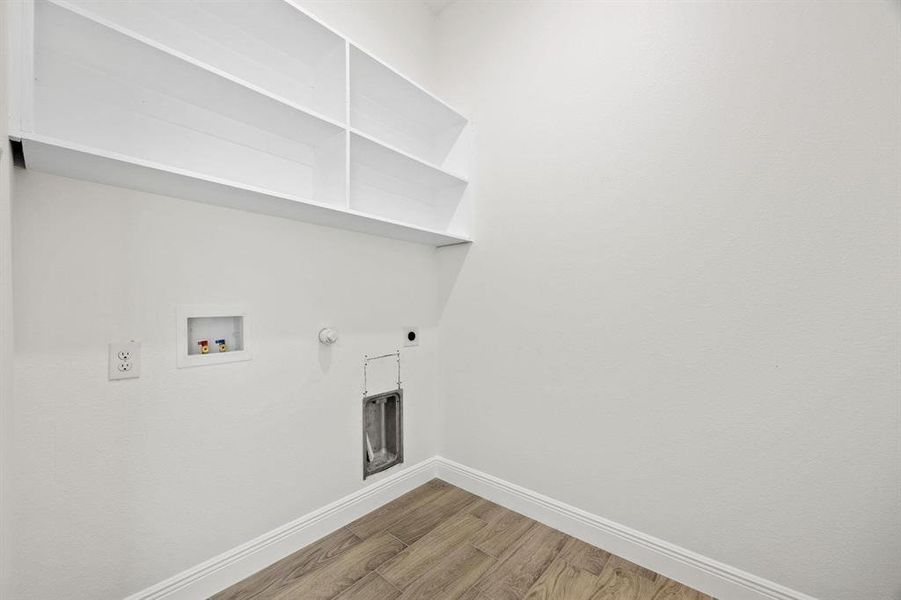 Dedicated laundry area featuring white built-in shelving, wood-finish flooring, white baseboards, and white walls Dedicated laundry area featuring white built-in shelving, wood-finish flooring, white baseboards, and white walls