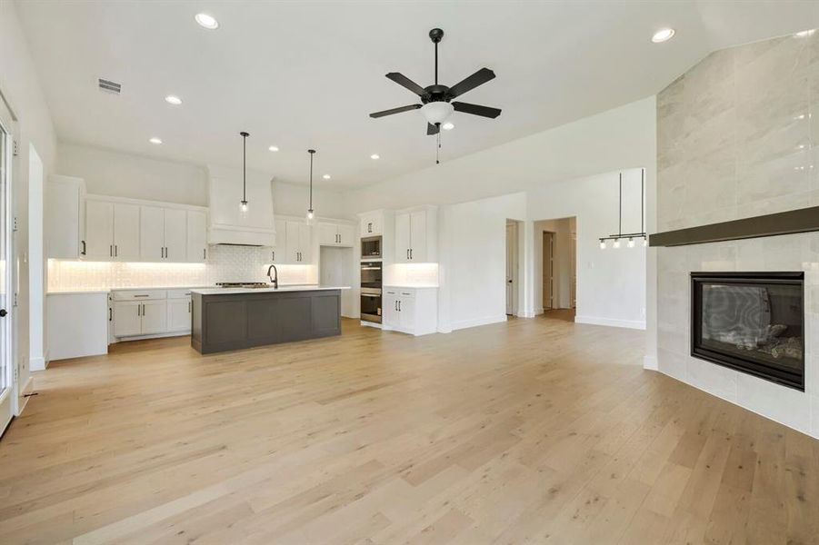 Open-concept living space featuring wood-finish flooring, a contemporary fireplace with a tile surround, and a kitchen island with pendant lighting Open-concept living space featuring wood-finish flooring, a contemporary fireplace with a tile surround, and a kitchen island with pendant lighting