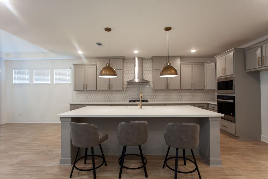 A showstopping island kitchen built for gatherings — seating for three, professional-grade gas cooktop, stainless chimney hood, double subway tile backsplash, and warm brass accents throughout.