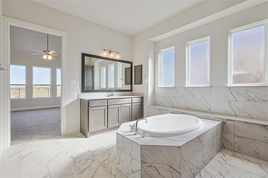 Bathroom with vanity, tiled bath, a wealth of natural light, and ceiling fan