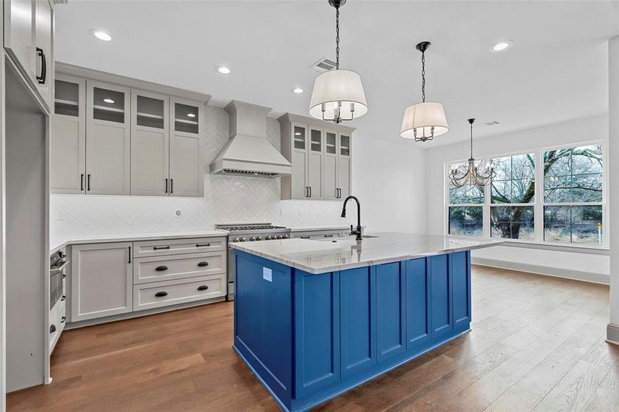 Kitchen featuring appliances with stainless steel finishes, decorative light fixtures, sink, light stone counters, and custom range hood