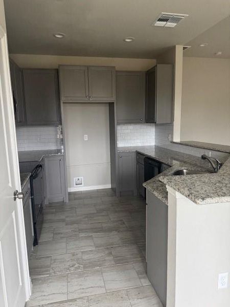 Kitchen with decorative backsplash, kitchen peninsula, gray cabinetry, sink, and range