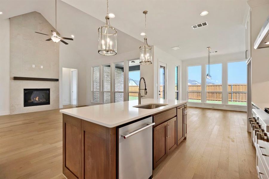 Kitchen with open floor plan, stainless steel appliances, light wood-style flooring, a tiled fireplace, and ceiling fan
