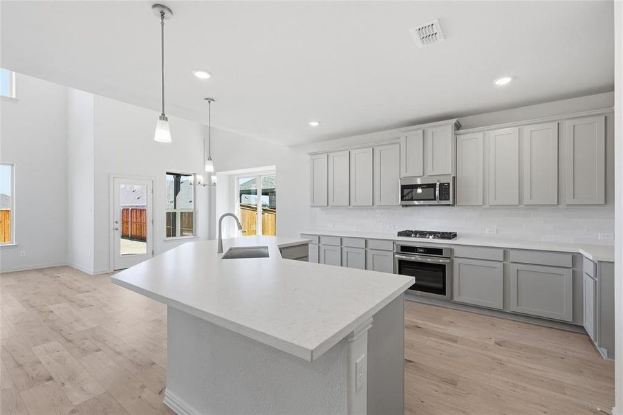 Kitchen featuring a central island with an undermount sink, pendant lighting, white countertops, light gray cabinetry, and a stainless steel oven/range and microwave