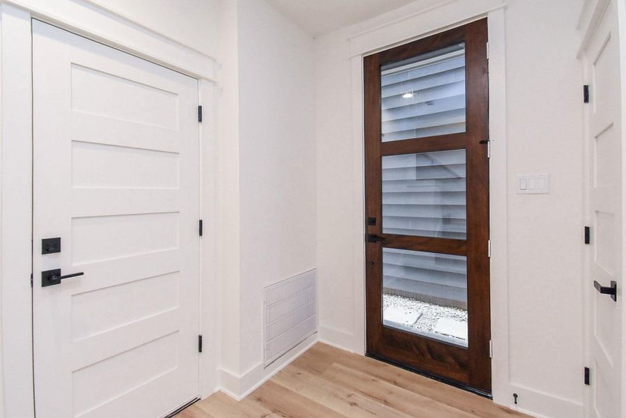 This entryway features a modern wooden door with glass panels, complemented by light-colored walls and flooring. It offers a clean, contemporary look with ample natural light.