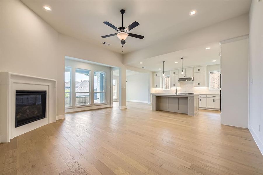 Unfurnished living room featuring a ceiling fan, light wood finished floors, recessed lighting, and a glass covered fireplace