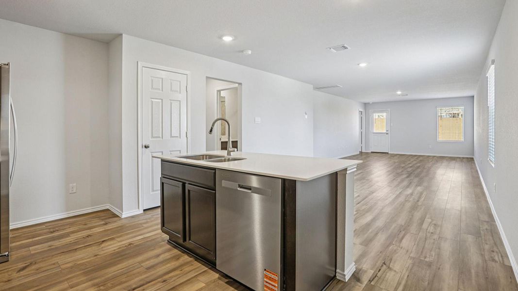 Kitchen featuring stainless steel appliances, open floor plan, a kitchen island with sink, dark wood finish cabinetry, and light wood-type flooring
