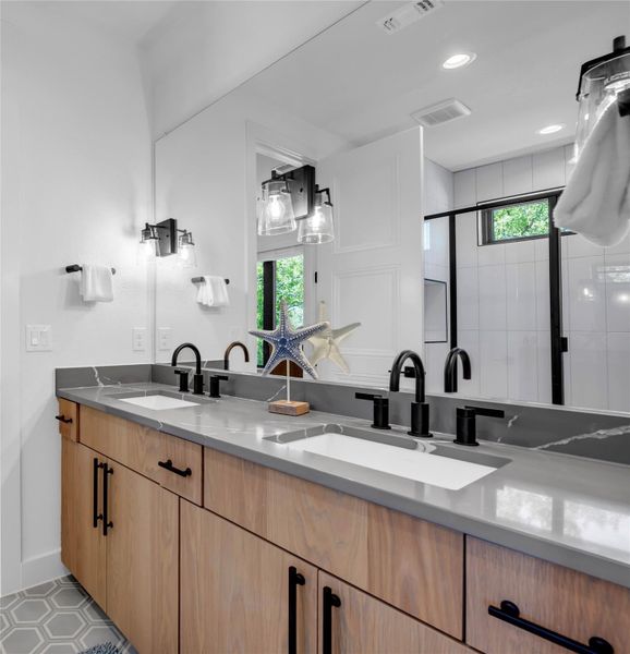 Bathroom four: Dual vanity with light wood-finish cabinetry, matte black hardware, and integrated sinks
