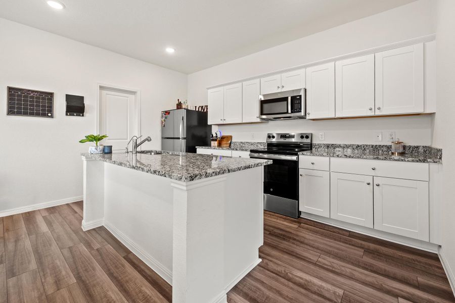 Kitchen featuring a central island with an undermount sink, granite countertops, white cabinetry, and stainless steel appliances.